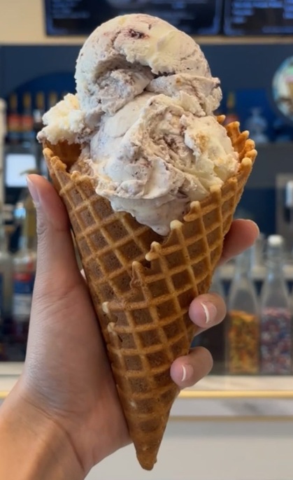 Two scoops of Blackberry Cheesecake ice cream in a waffle cone.